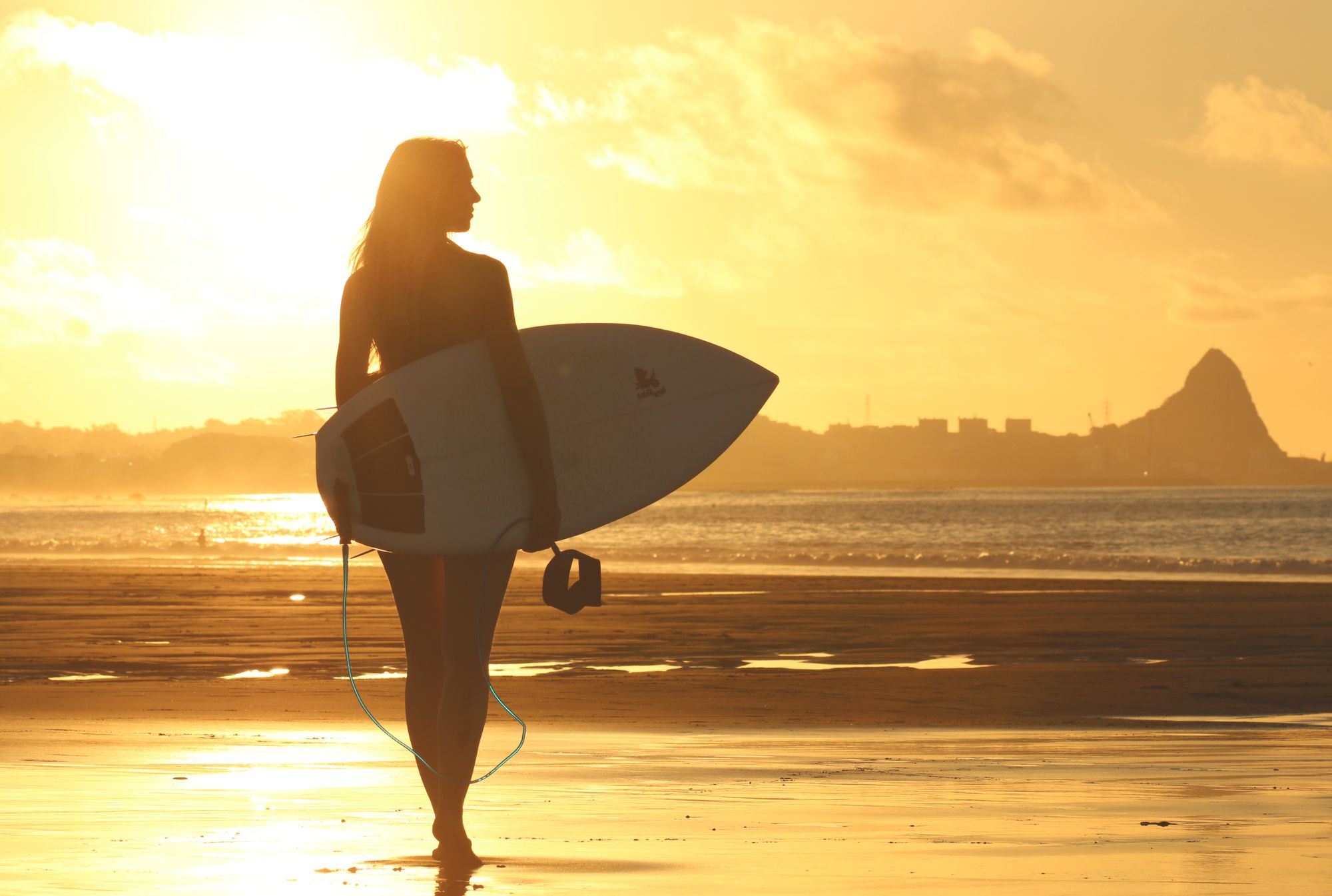 Girl holding a surfboard at an ocean sunset
